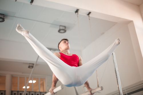 Free A skilled male gymnast demonstrates control and strength on gymnastic rings indoors. Stock Photo