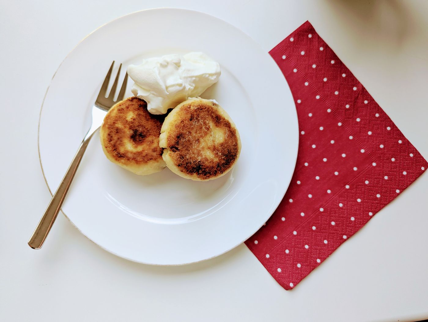 Enjoy a delightful breakfast featuring golden pancakes with cream, elegantly presented on a white plate with a fork.