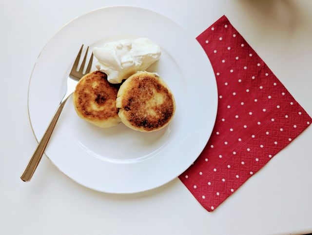 Enjoy a delightful breakfast featuring golden pancakes with cream, elegantly presented on a white plate with a fork.