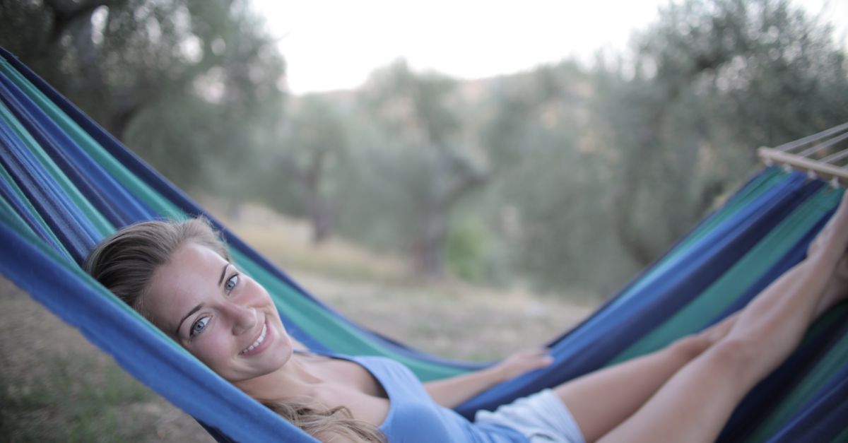 young woman lying in a hammock with a book, looking relaxed and happy, natural lighting