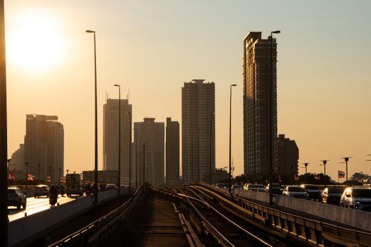 Silhouette of Bangkok skyscrapers and bridge at sunset with urban traffic.