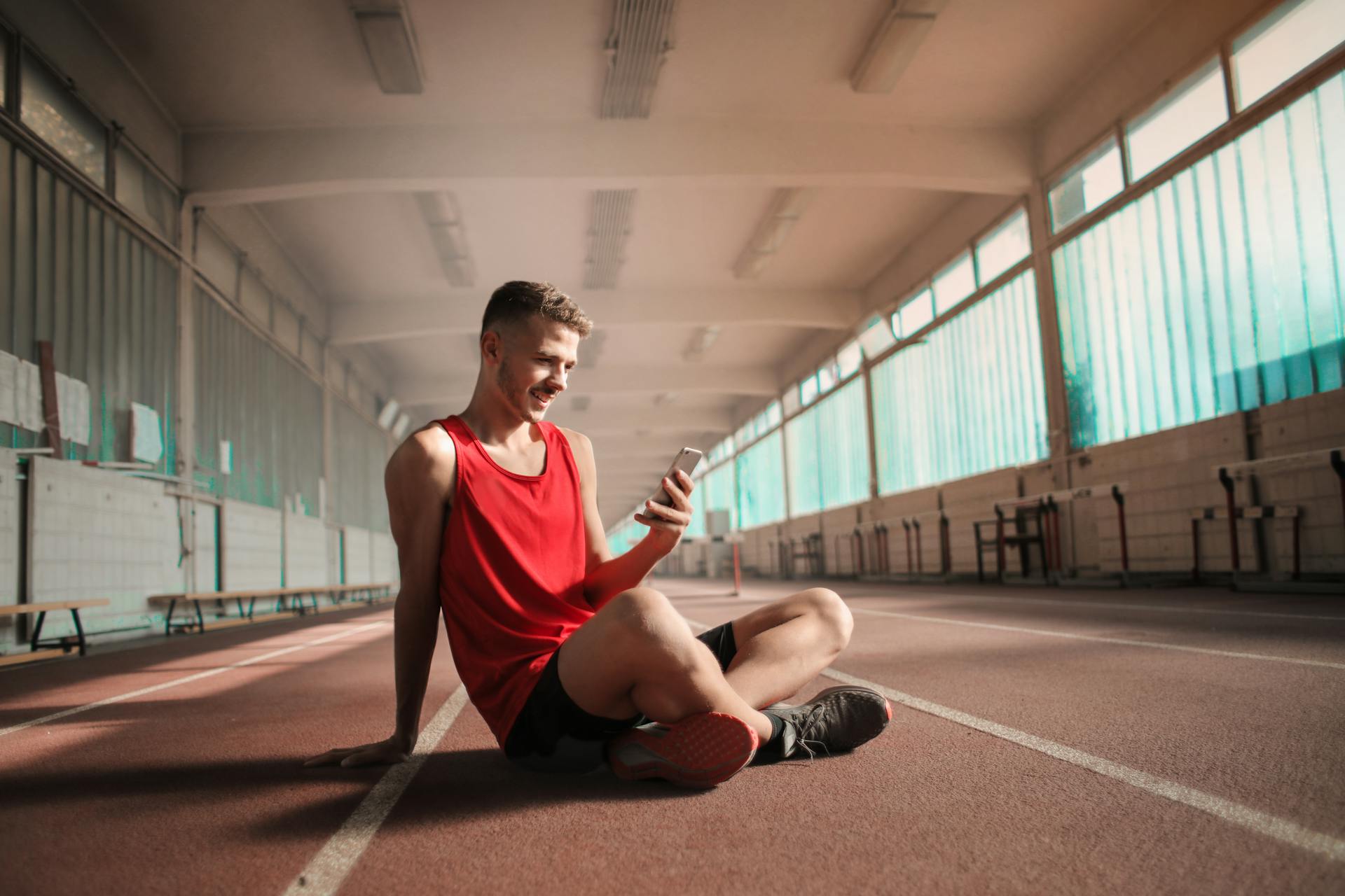 Smiling athlete in activewear sitting on track, texting on smartphone.