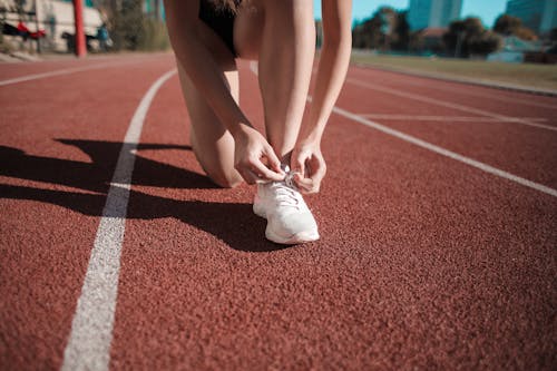 女人在跑道上綁她的白色運動鞋的特寫照片