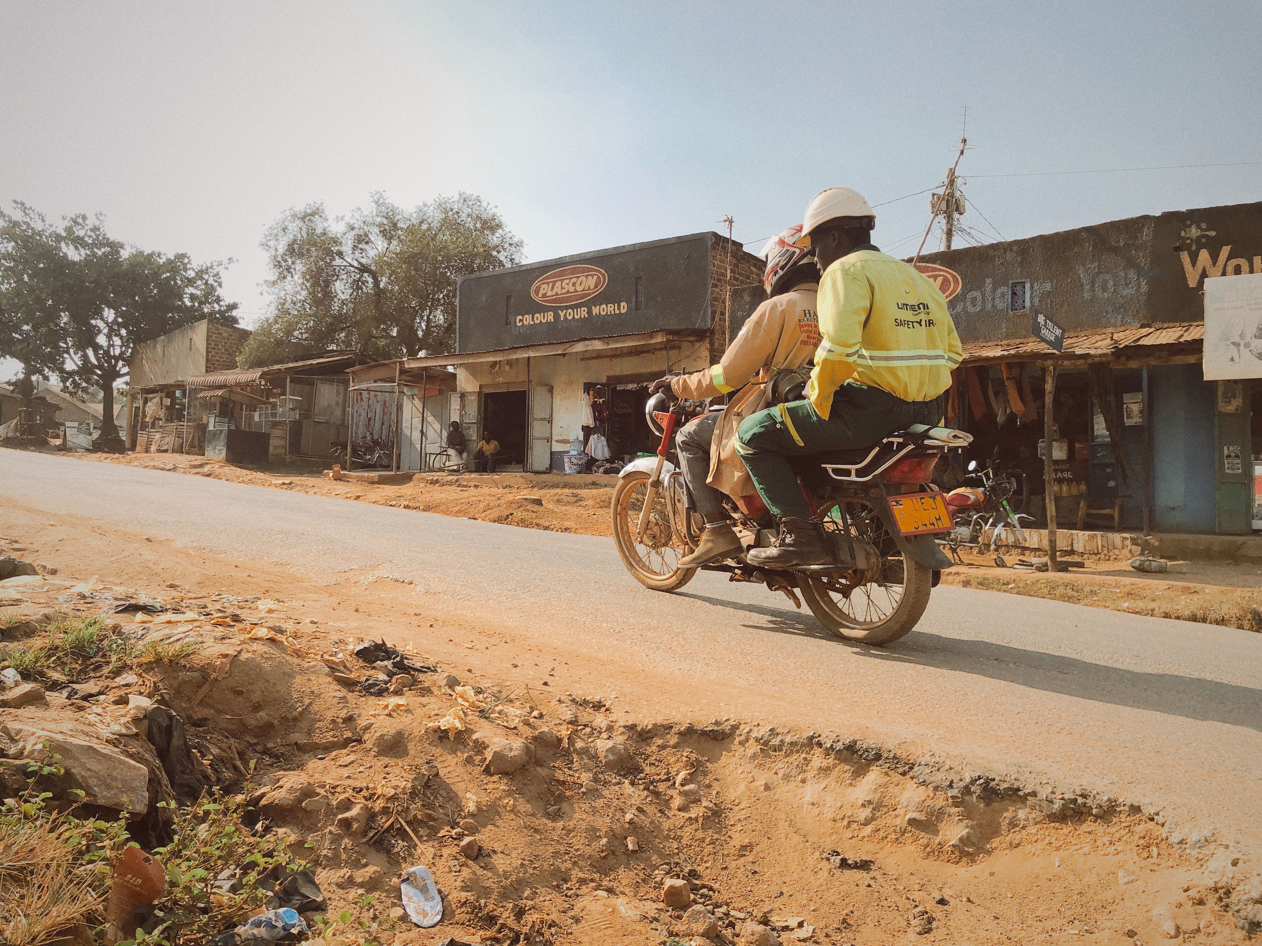 ingyenes Két motoros halad egy poros úton egy kis ugandai városban, amelyet helyi üzletek szegélyeznek. Stockfotó