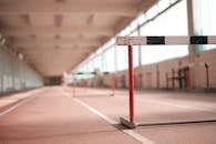 Hurdle painted in white black and red colors placed on empty rubber running track in soft focus