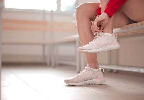 A young woman in a red sweater ties her sneakers while sitting on an indoor bench.