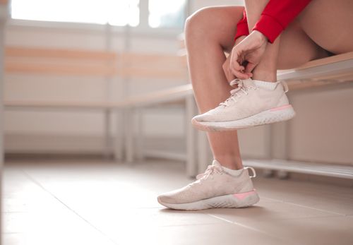 Free A young woman in a red sweater ties her sneakers while sitting on an indoor bench. Stock Photo