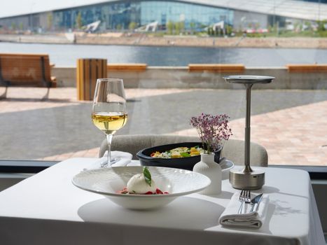 A restaurant table with wine and dishes overlooking a scenic waterfront view.