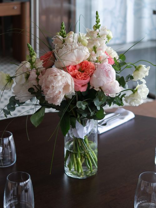 Free A beautiful bouquet of peonies in a glass vase on a dining table with soft lighting. Stock Photo