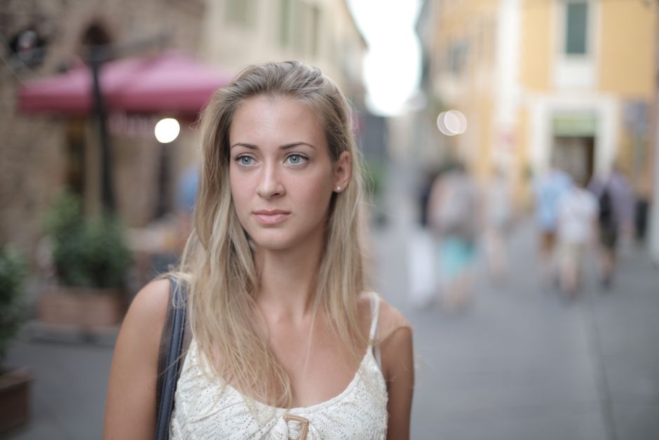 Elegant portrait of a woman with blonde hair, standing in a lively street setting.