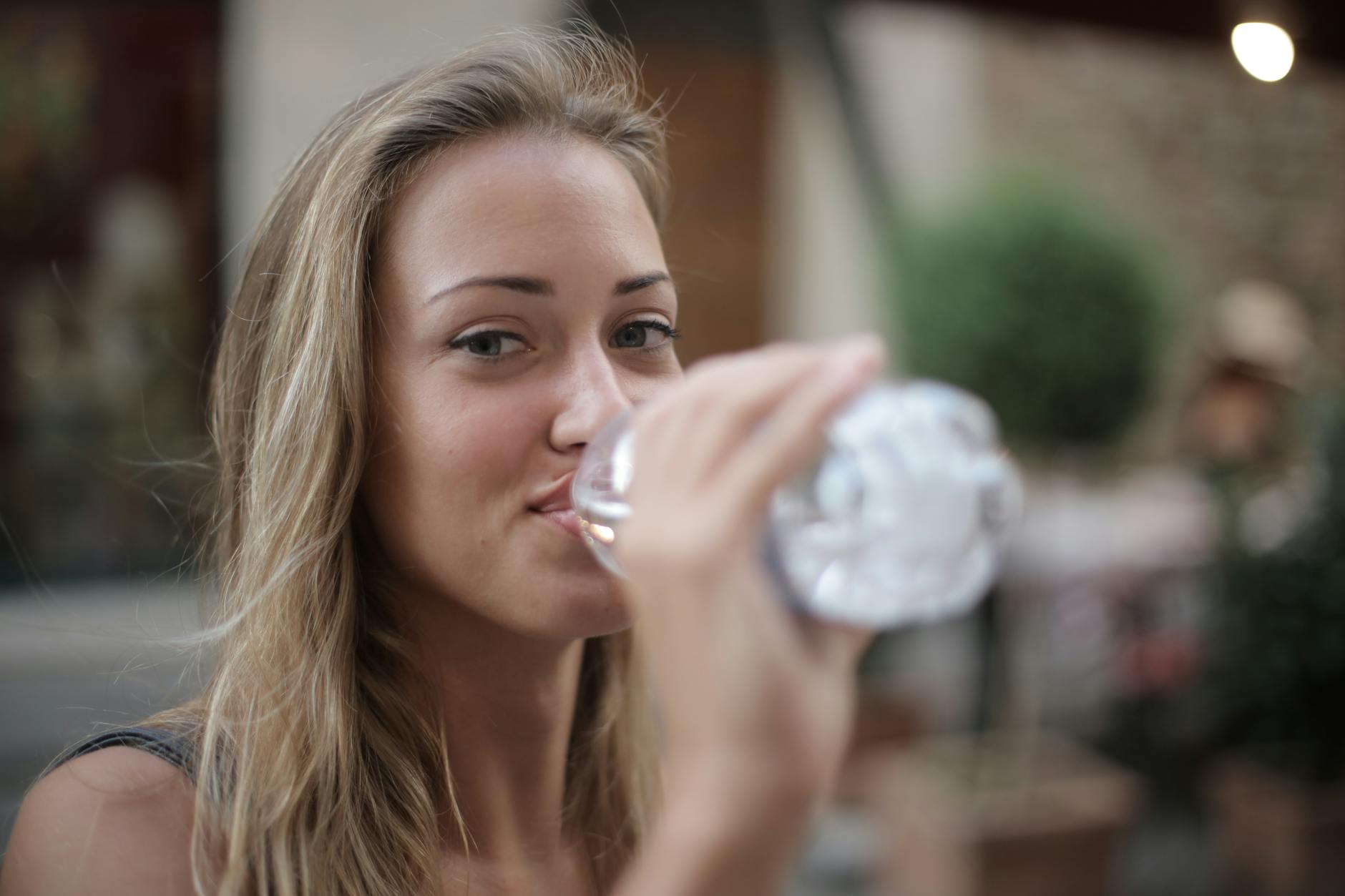 Mulher bebendo água na garrafa pet olhando para a câmera. Beber água é primordial para ter uma alimentação saudável!