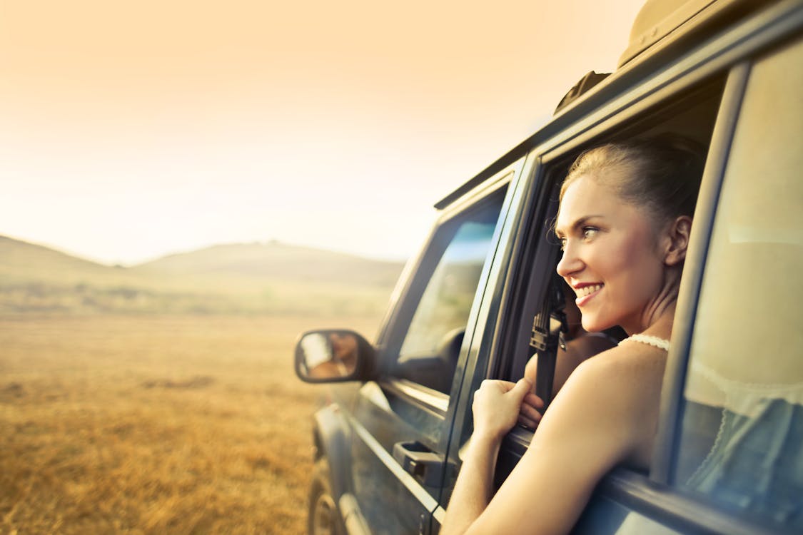 Young happy female smiling and enjoying sunset through open window while traveling by car