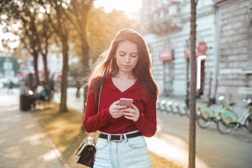Free A young woman in casual wear using her smartphone on a sunny day in the city. Stock Photo