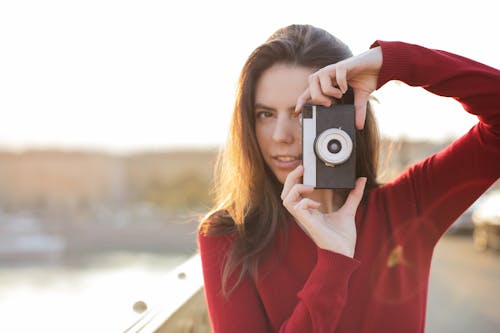 Selective Focus Portrait Photo of Woman in Red Long Sleeve Sweater Taking a Photo with a Camera