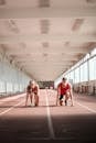 Couple of professional sportspeople ready for sprinting on empty track in training hall on sunny day