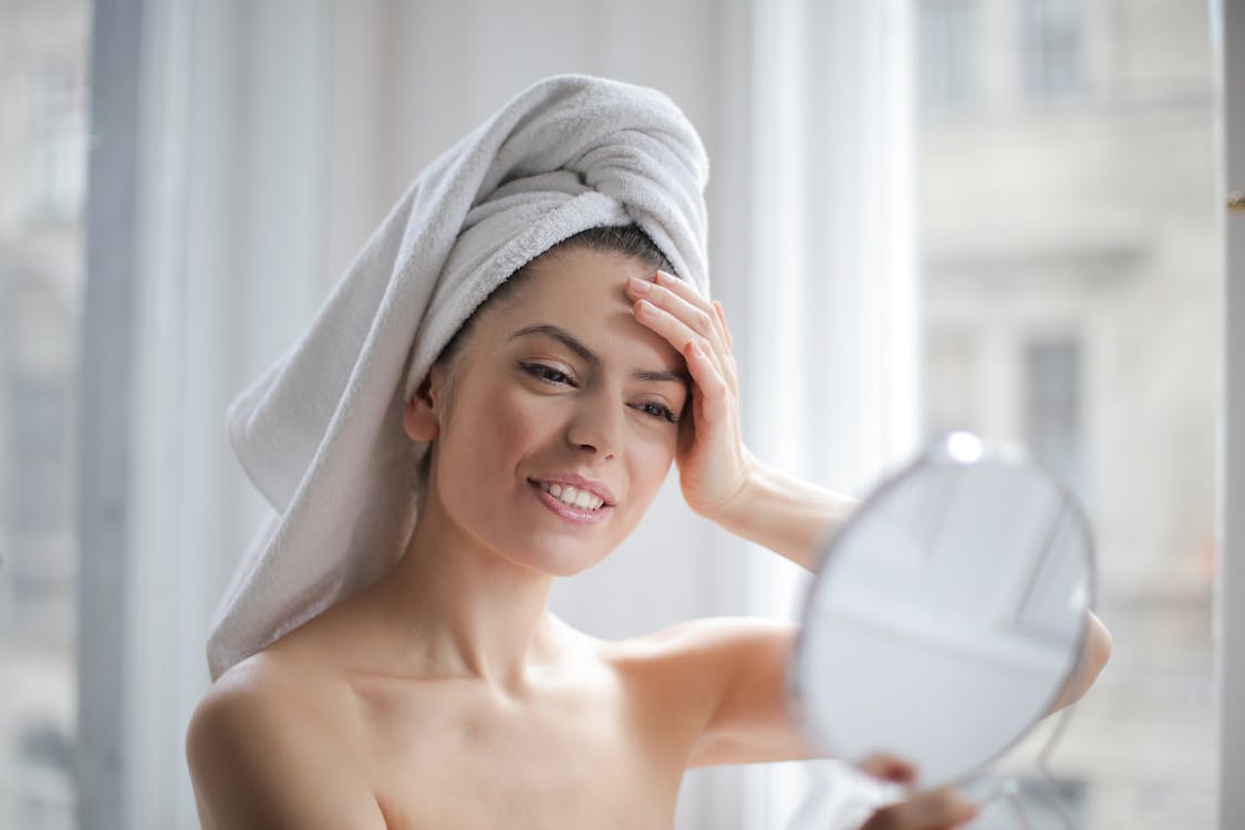 Free Selective Focus Portrait Photo of Smiling Woman With a Towel on Head Looking in the Mirror Stock Photo
