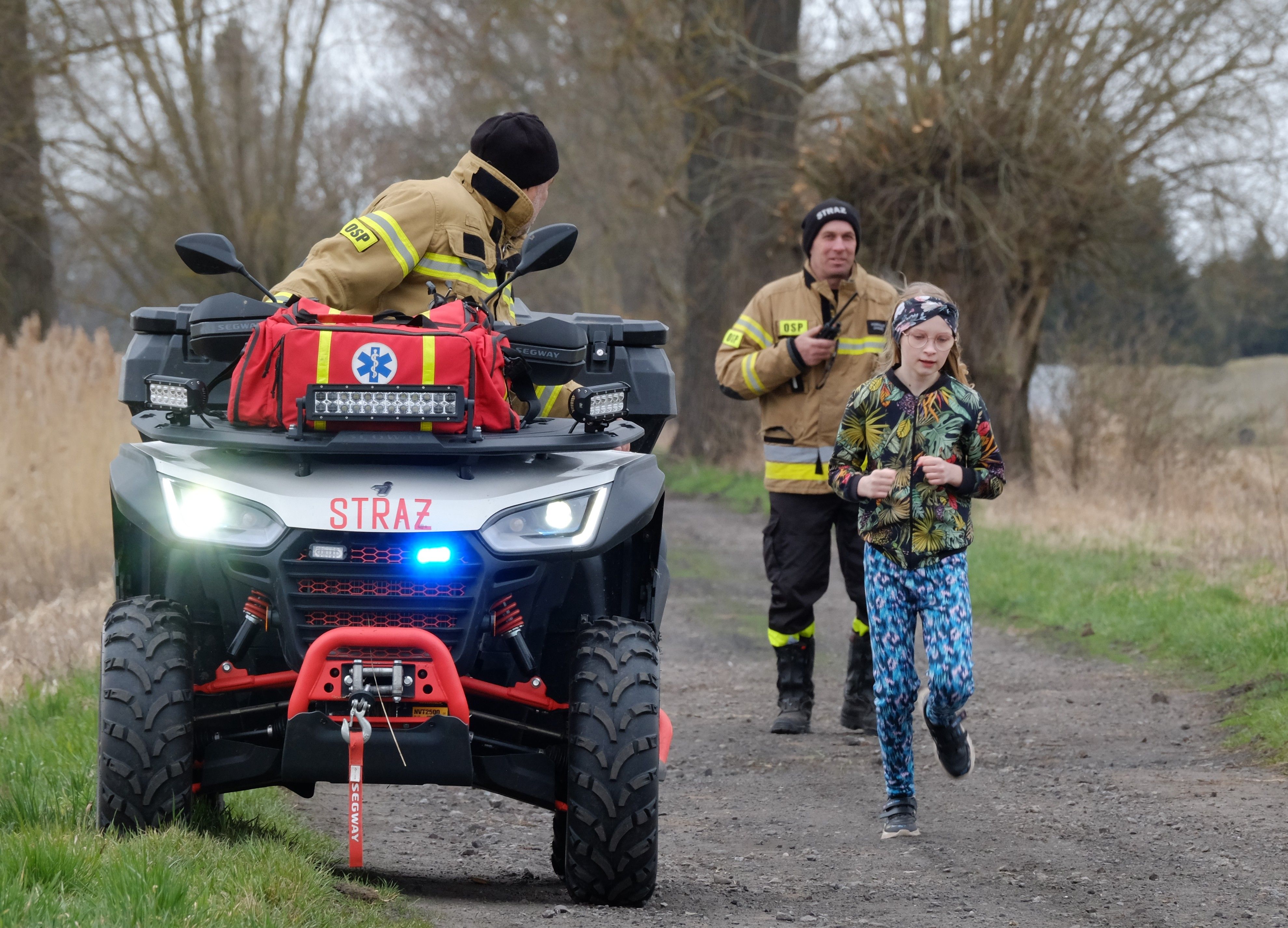 Firefighters on an ATV accompany a running child on a rural path, symbolizing community safety.