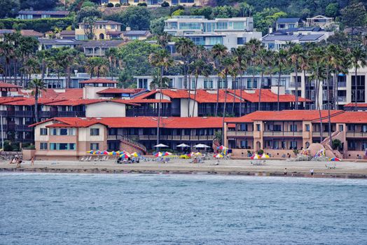 Colorful umbrellas line the sandy San Diego beach, framed by charming coastal architecture.
