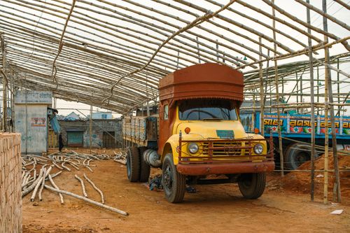 Free A rustic yellow truck parked inside a partially built bamboo structure, capturing a unique industrial scene. Stock Photo