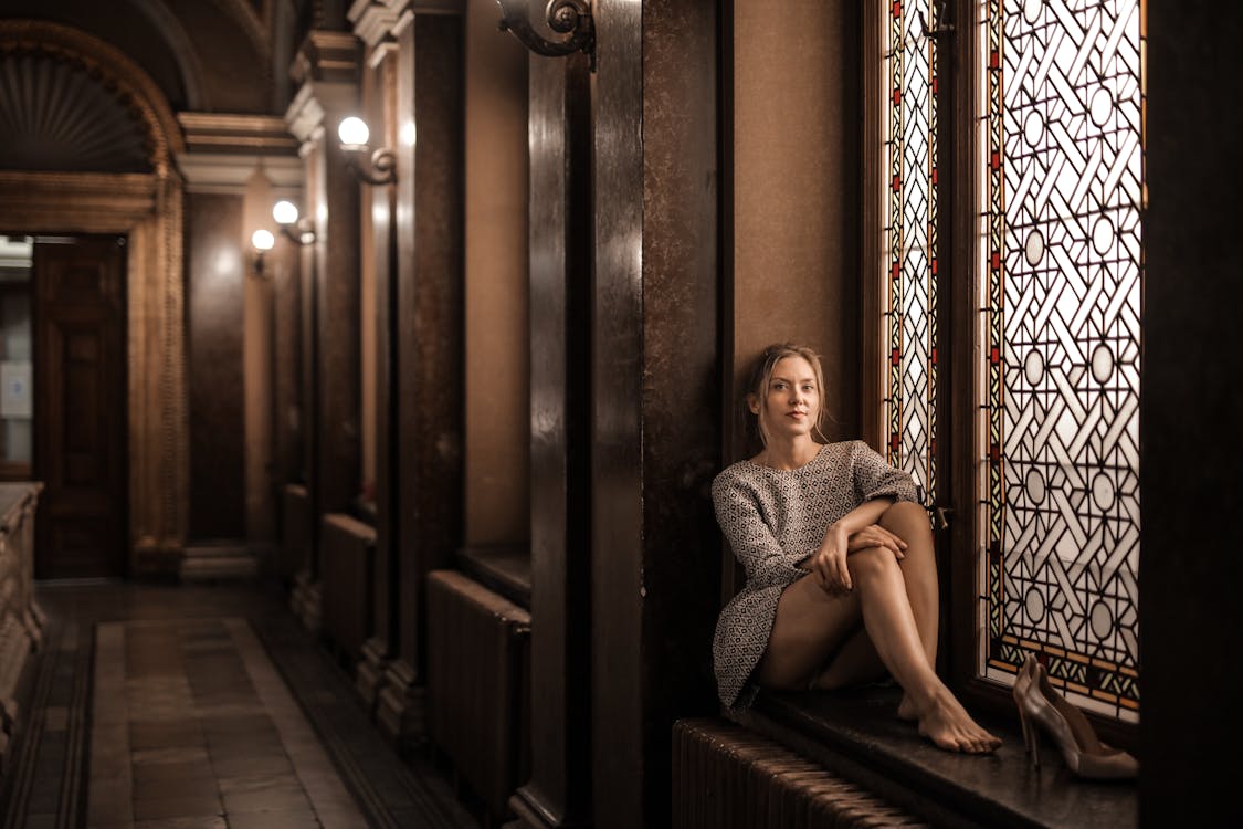 Free Blonde barefoot female sitting by painted window in dark lobby with Gothic interior Stock Photo