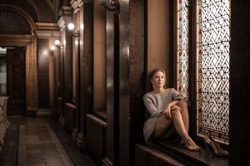 Free Blonde barefoot female sitting by painted window in dark lobby with Gothic interior Stock Photo