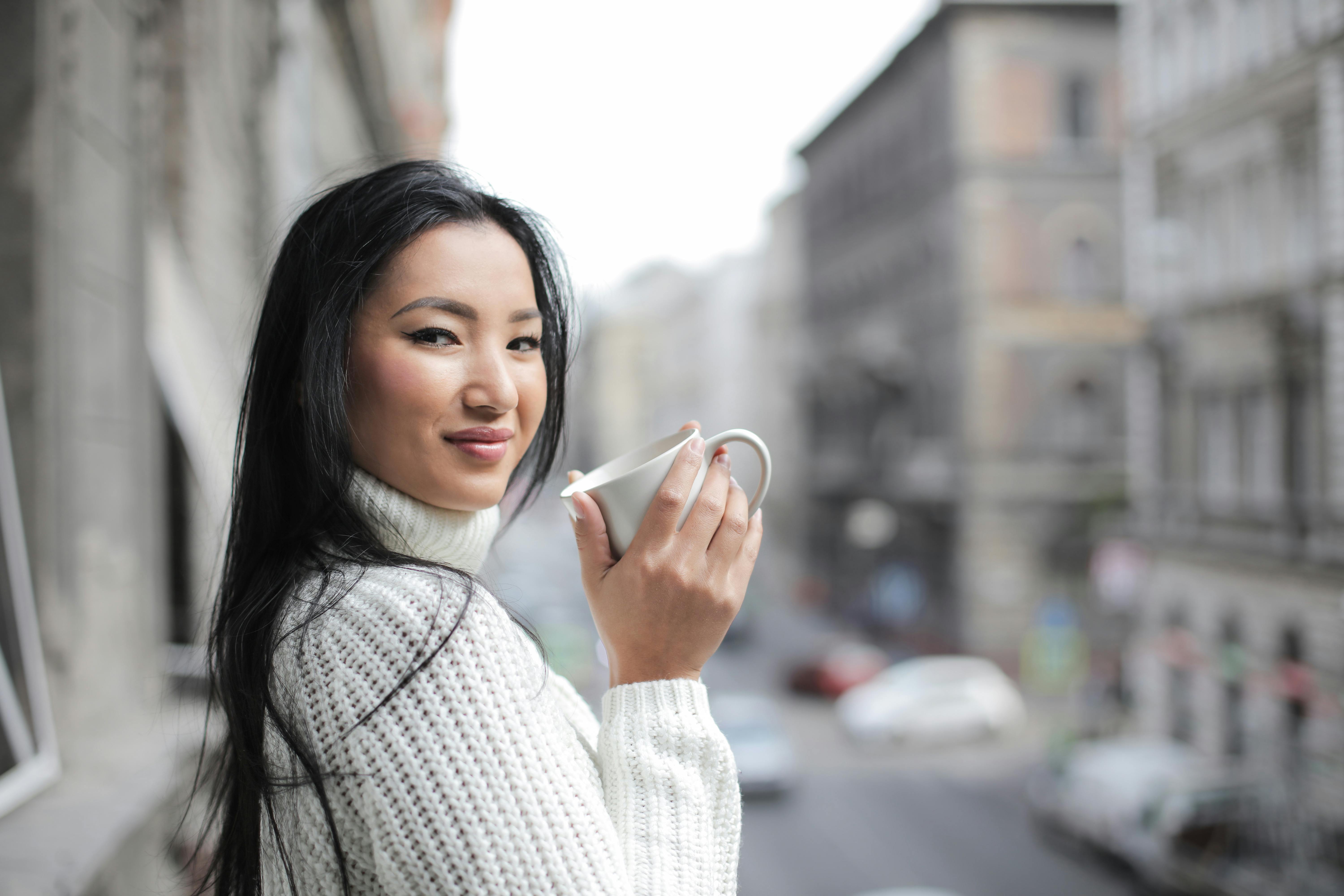 一名女子穿着针织衫，在城市背景下喝着咖啡
