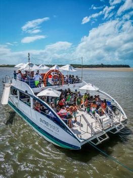 A vibrant excursion boat filled with tourists exploring the waters of Tibau do Sul, Brazil.