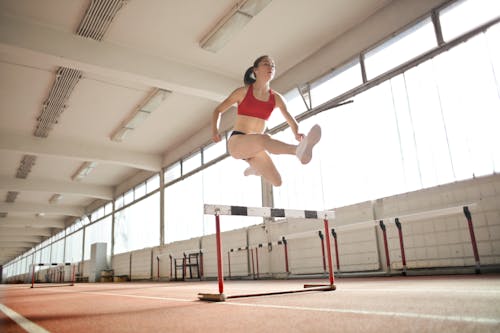 Woman in Red Sports Bra Jumping on White and Black Obstacle