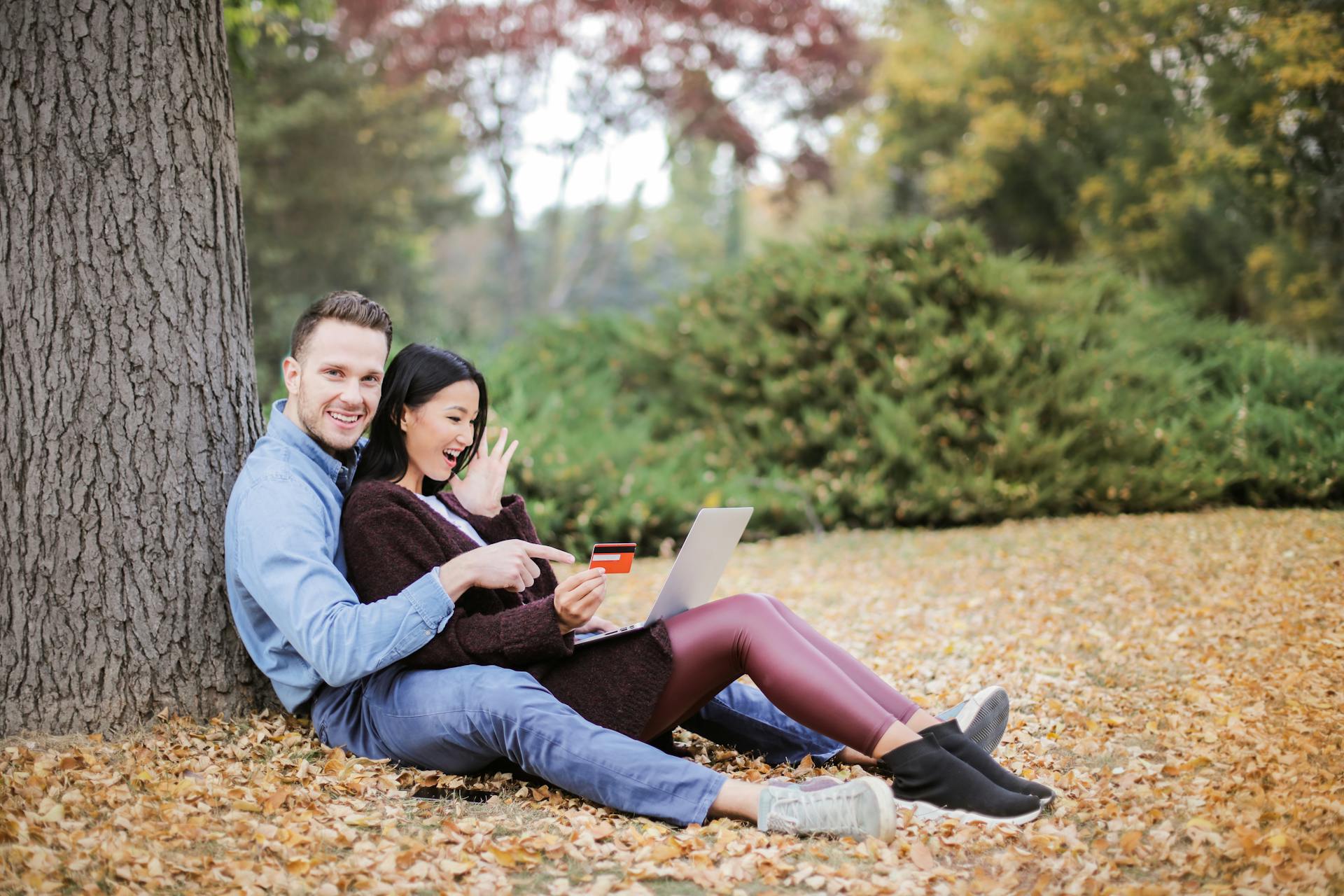 A joyful couple using a laptop and credit card outdoors during fall.