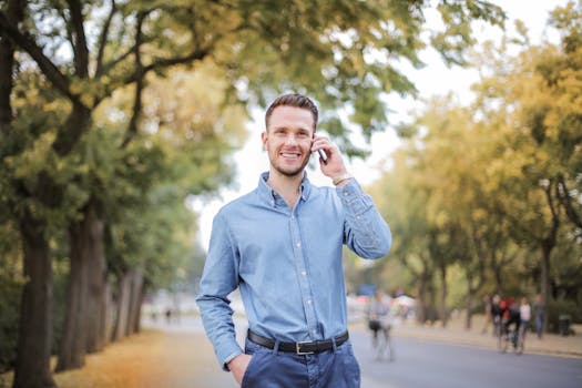 在一个阳光明媚的日子里，一位穿着休闲服的开朗男子正在户外用智能手机通话