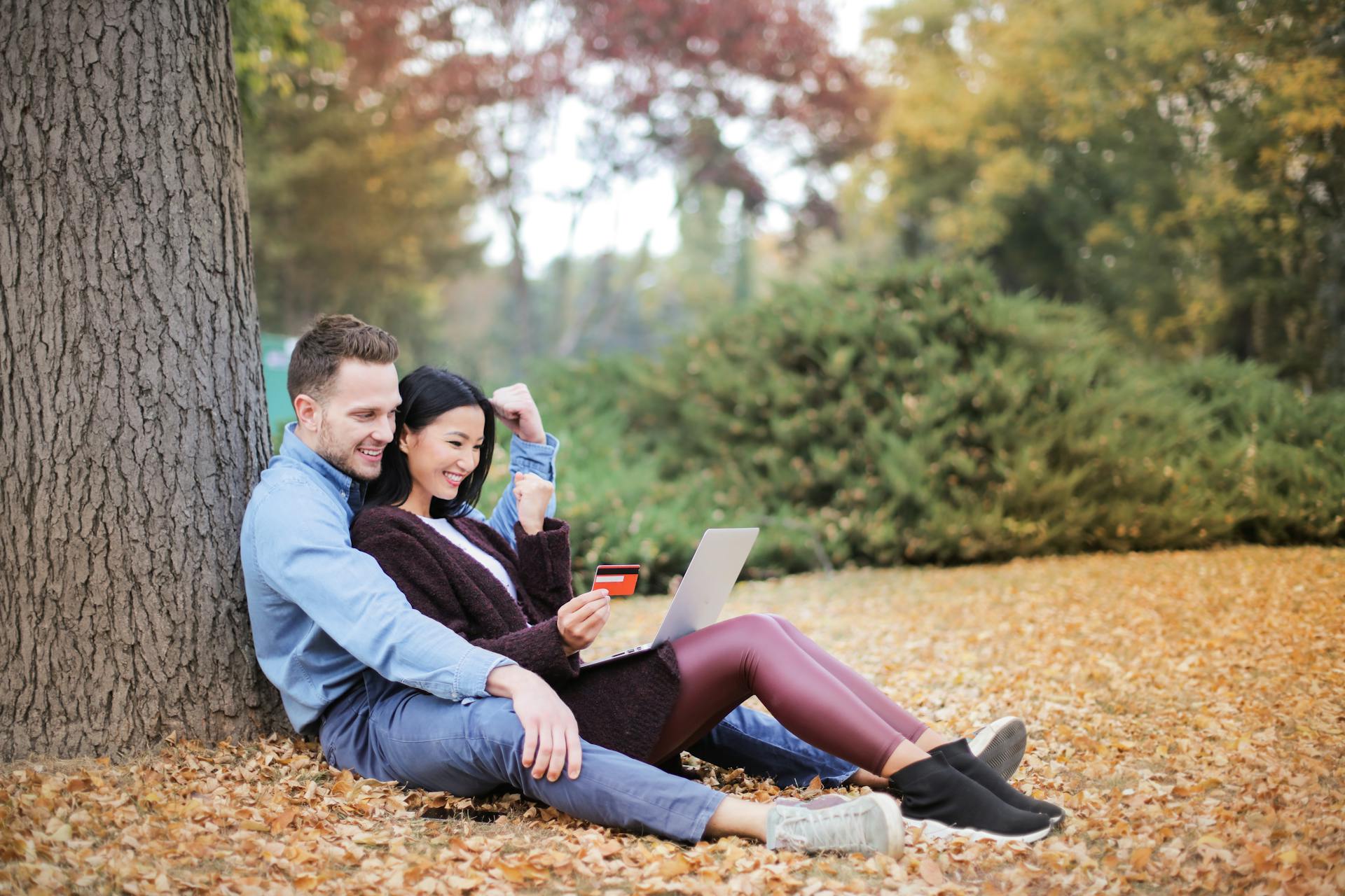 Happy couple outdoors shopping online with a laptop during fall.