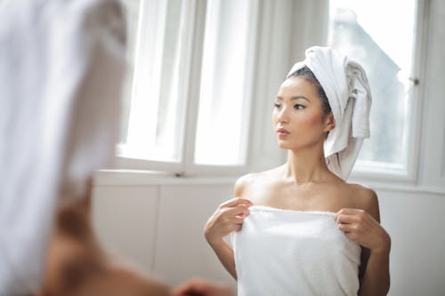 Free Back View Photo of Woman in White Towel Standing In Front of a Mirror Stock Photo