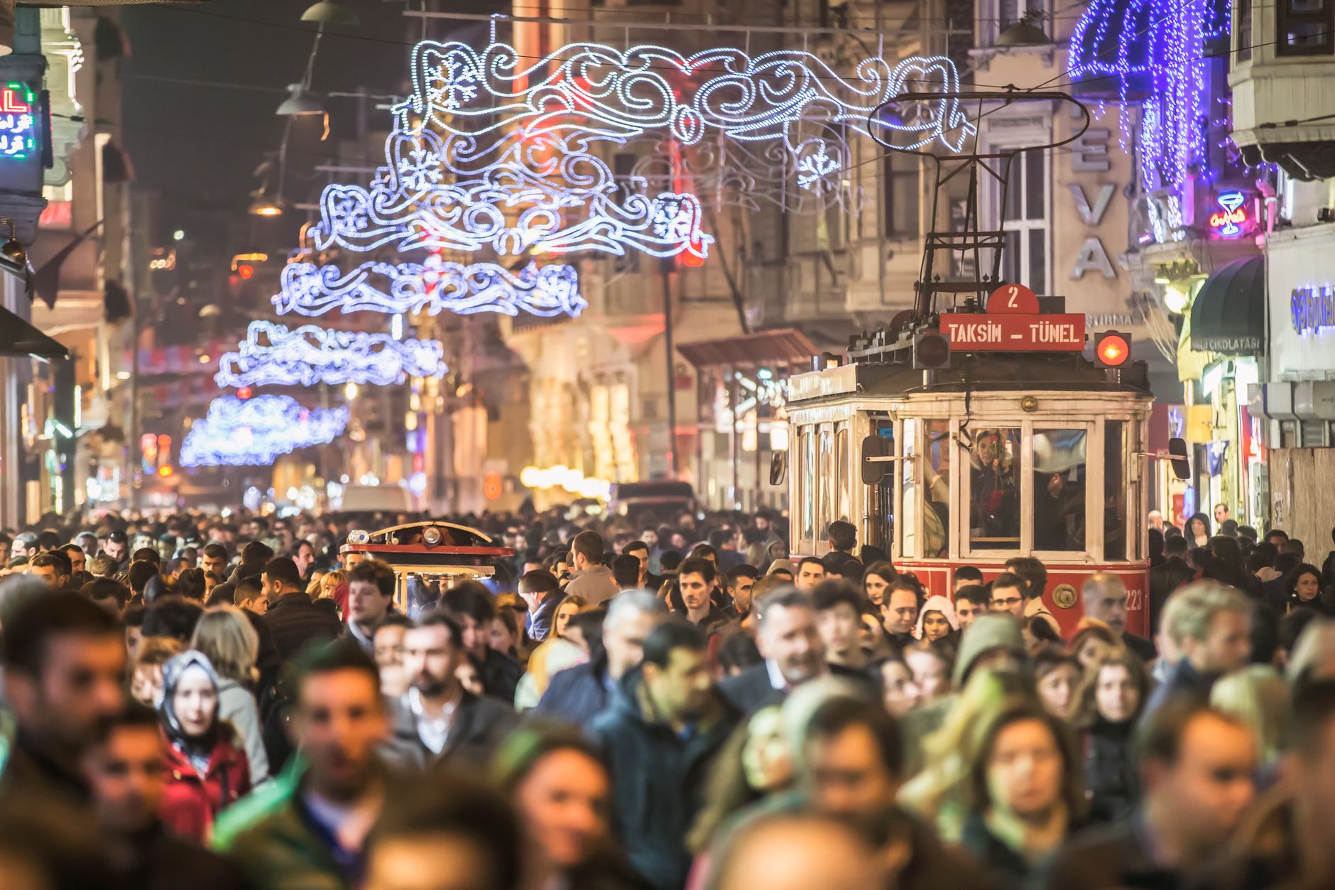 A bustling night scene on Istiklal Street, Istanbul, with festive lights and a historic tram among the crowd.