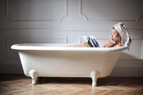 Фотография женщины в белой ванне читает журнал