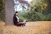 秋天，一名年轻女子在公园的树下用着笔记本电脑