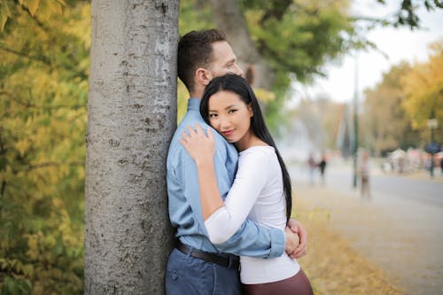 Selective Focus Photo of Hugging Couple Standing Next to a Tree