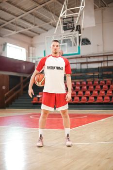 A basketball player poses on an indoor court, ready for practice or game.