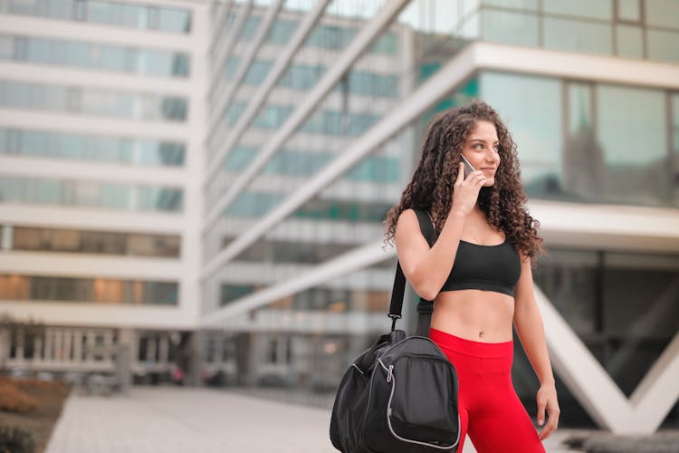 Selective Focus Photo Of Smiling Woman In Active Wear Carrying Gym Back While Talking On The Phone