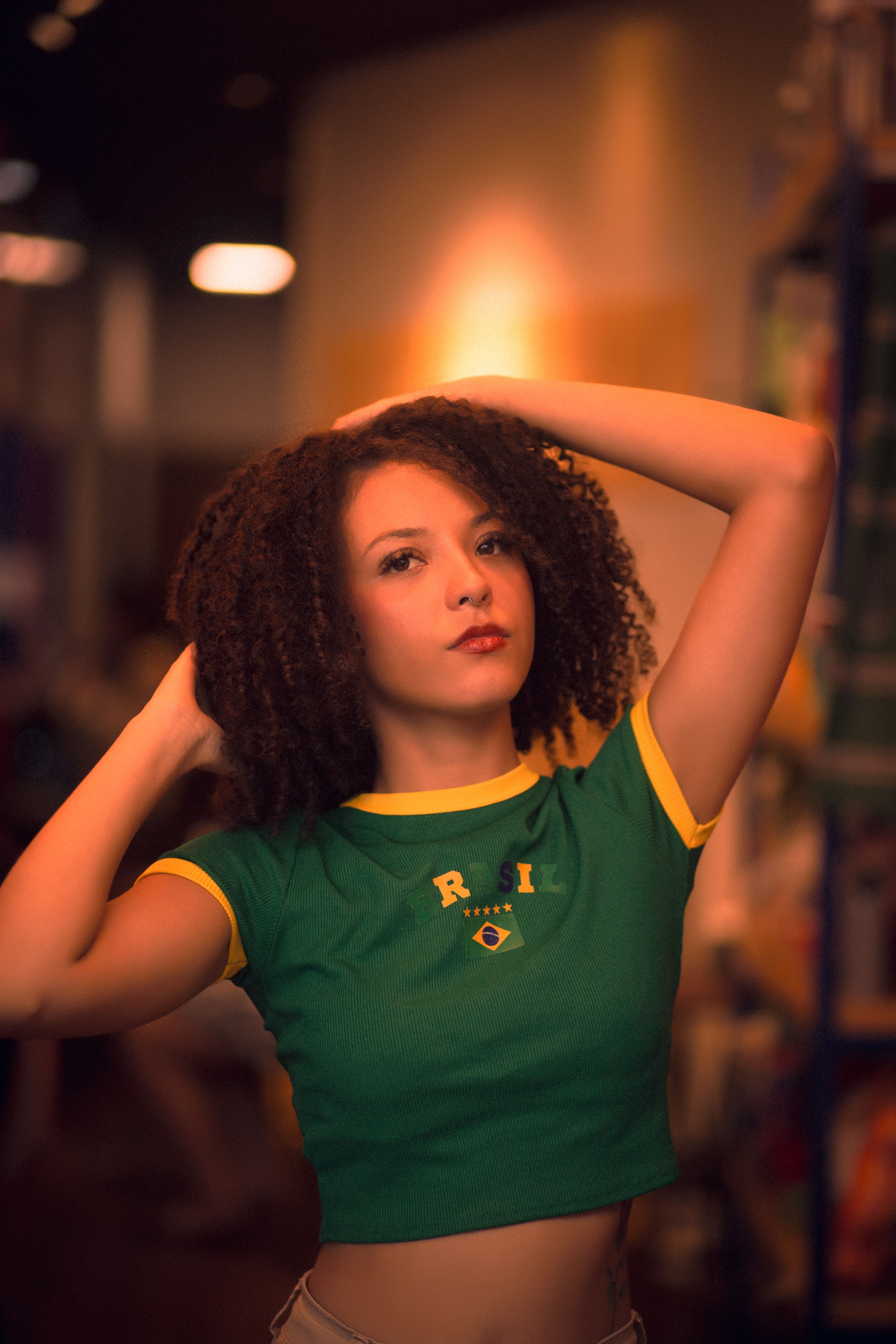 Portrait of a young woman in a Brazil jersey posing confidently indoors with a warm tone.