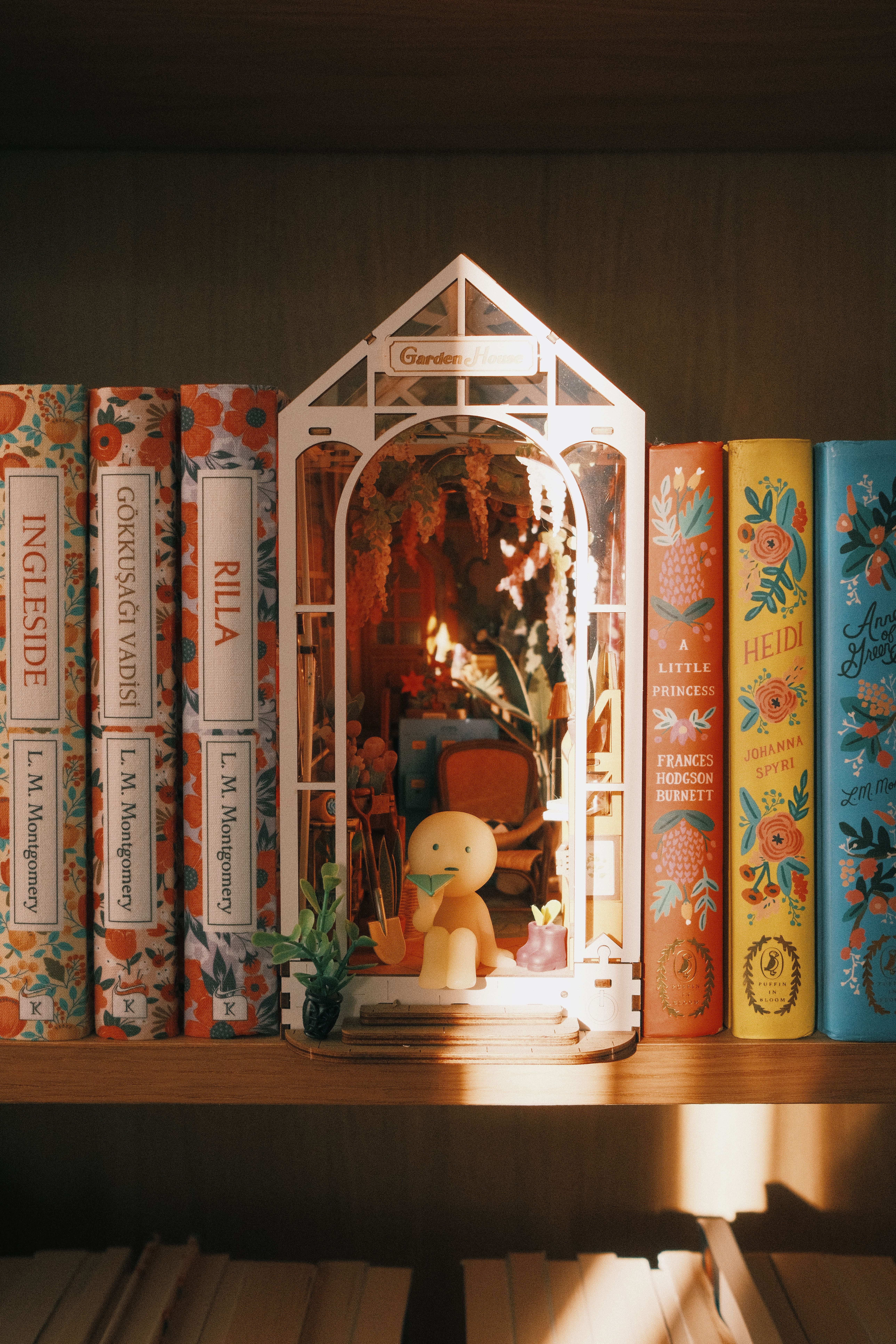 A vibrant bookshelf featuring classic literature and a charming miniature garden diorama.