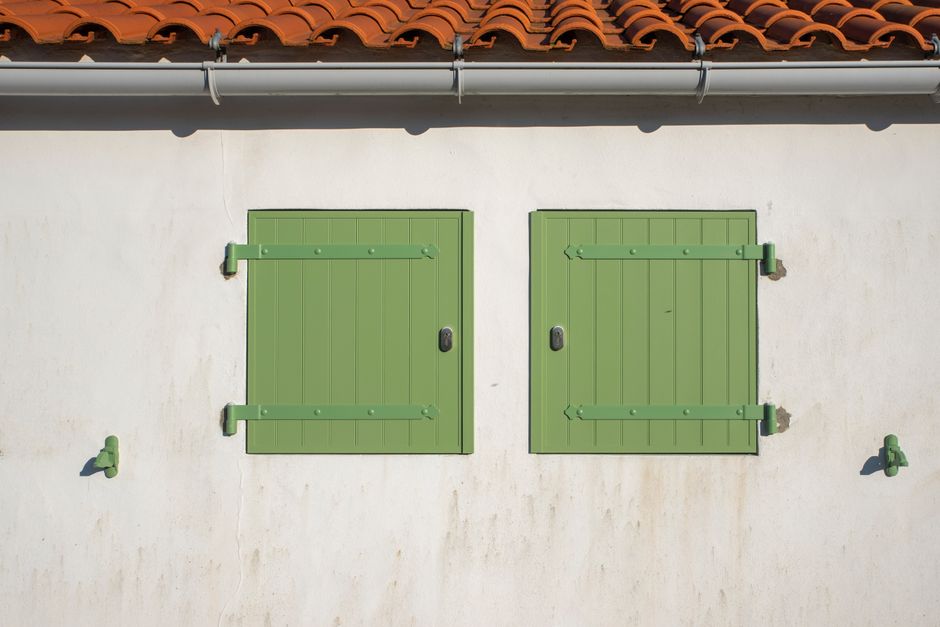 Minimalist facade with green shutters showcases Mediterranean design with terracotta roof tiles.