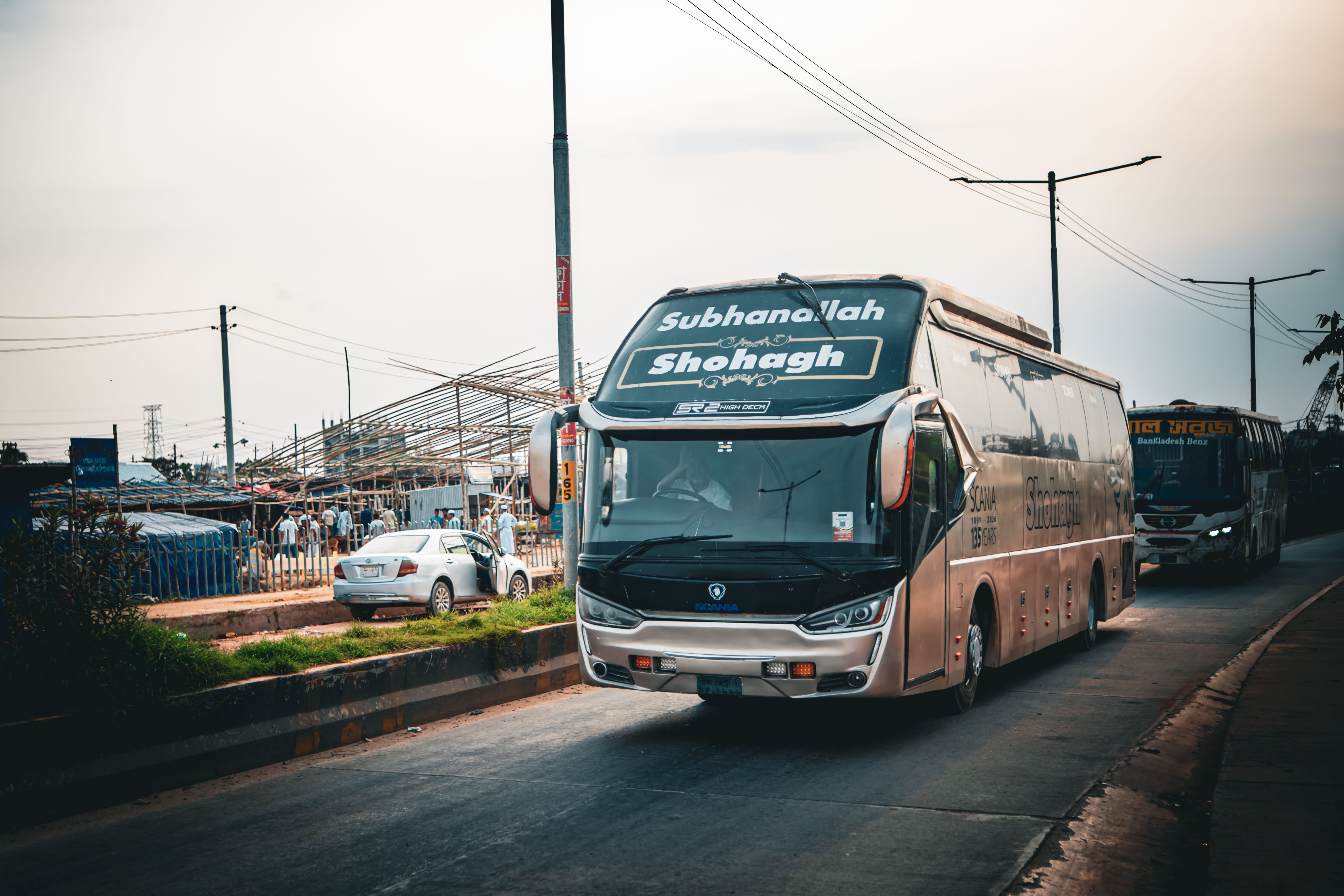 Un grande autobus cittadino viaggia su una strada affollata a Dacca, Bangladesh, sotto un cielo offuscato.