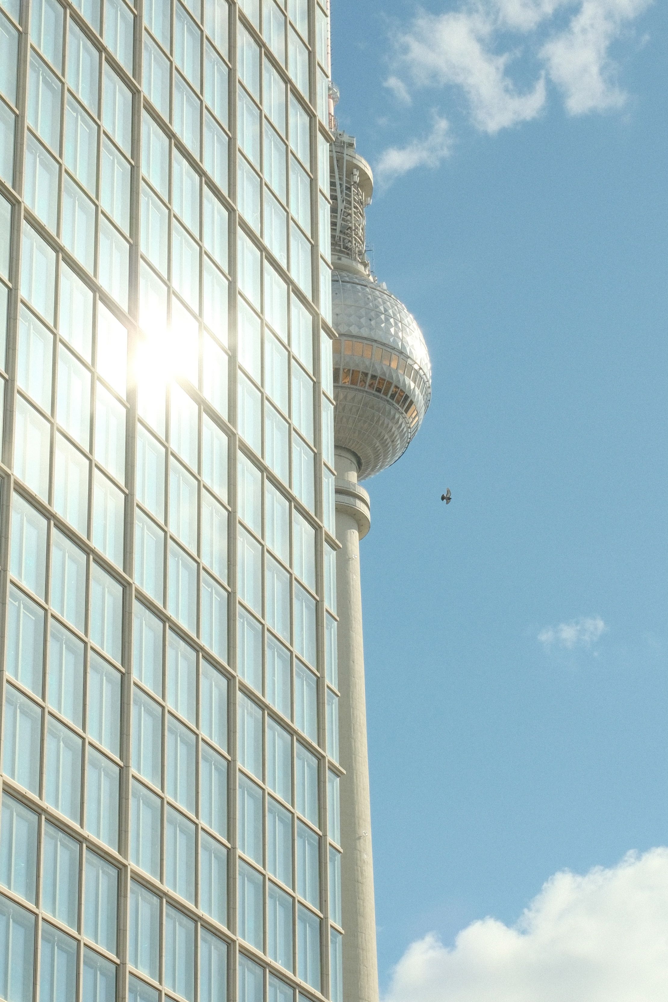 A stunning view of Berlin's TV Tower peeking behind a modern glass building on a clear day.