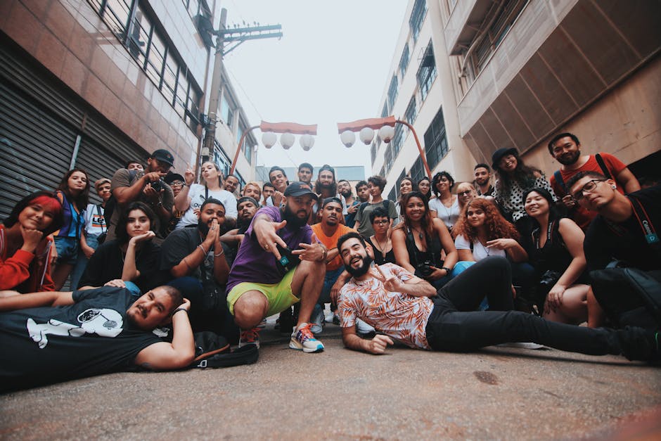 Group of young happy diverse friends sitting on ground on street and smiling while looking at camera