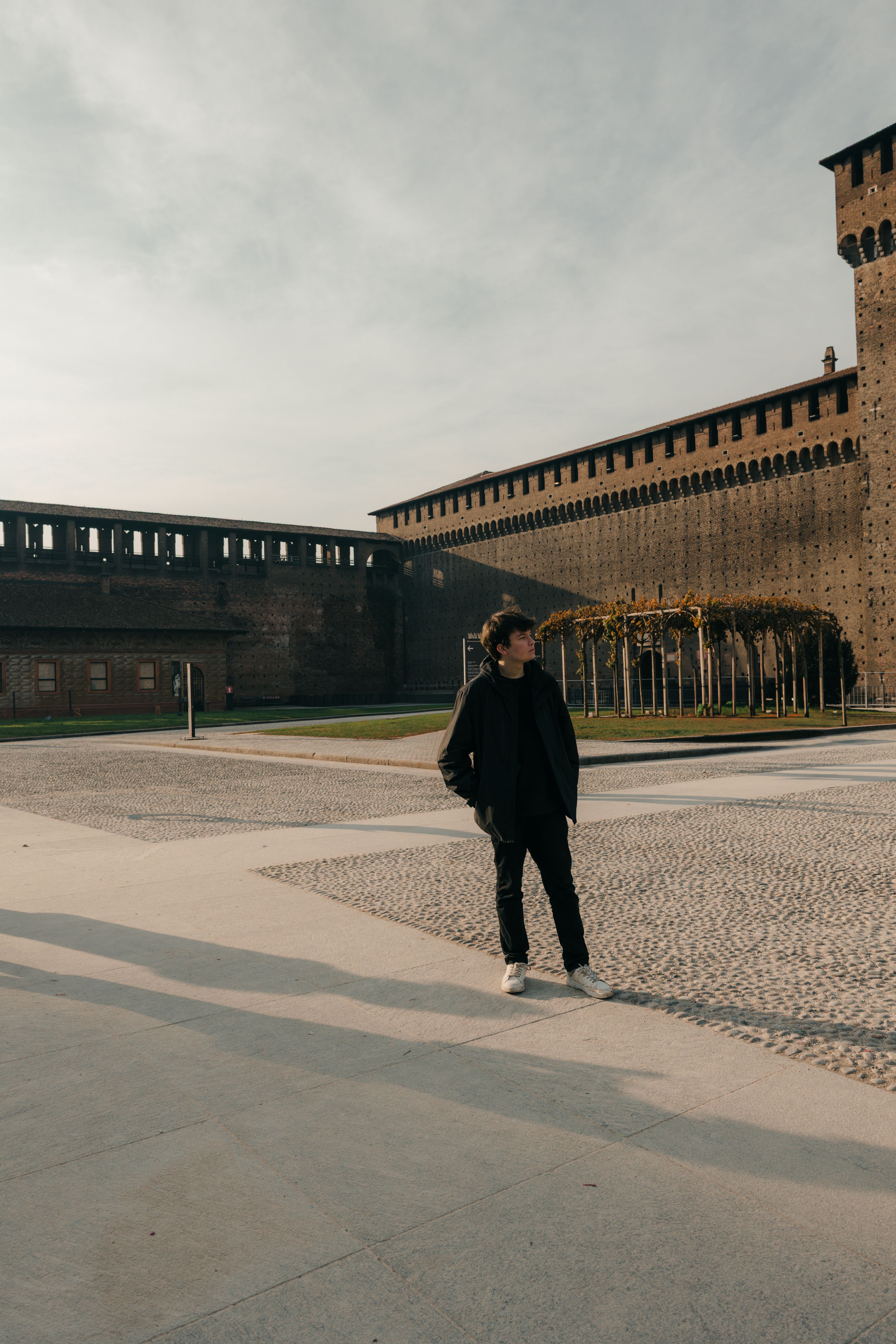 A young man walks beside the historic Sforza Castle in Milan, Italy, during the day.