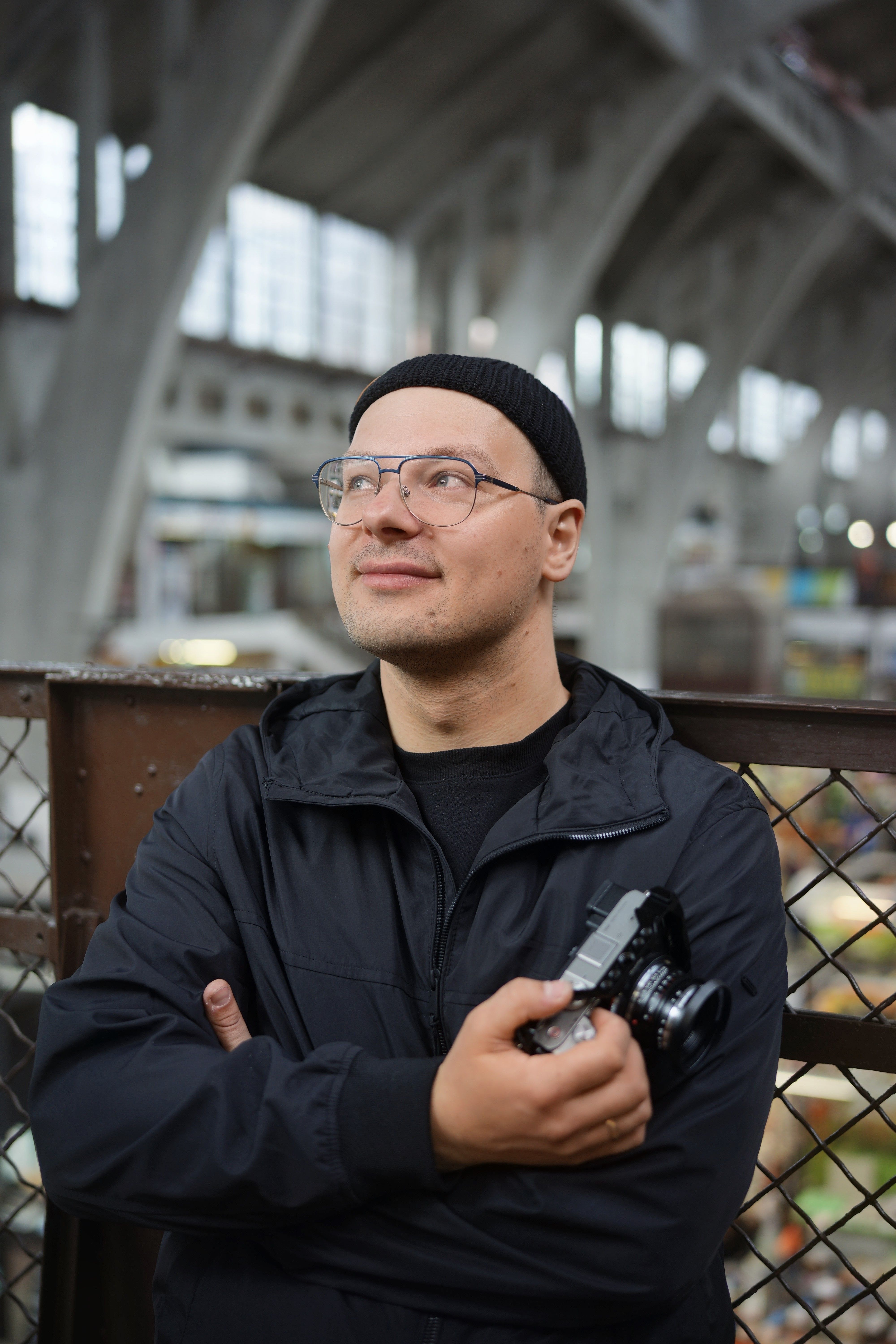 Man in black jacket and glasses holding camera at Wrocław indoor market.