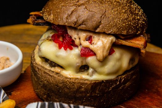 Close-up of a delicious homemade cheeseburger with bacon and peppers on a wooden board.
