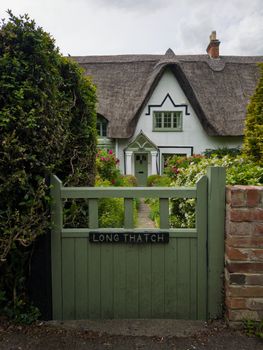 A picturesque thatched cottage surrounded by lush garden and greenery during summer in England.