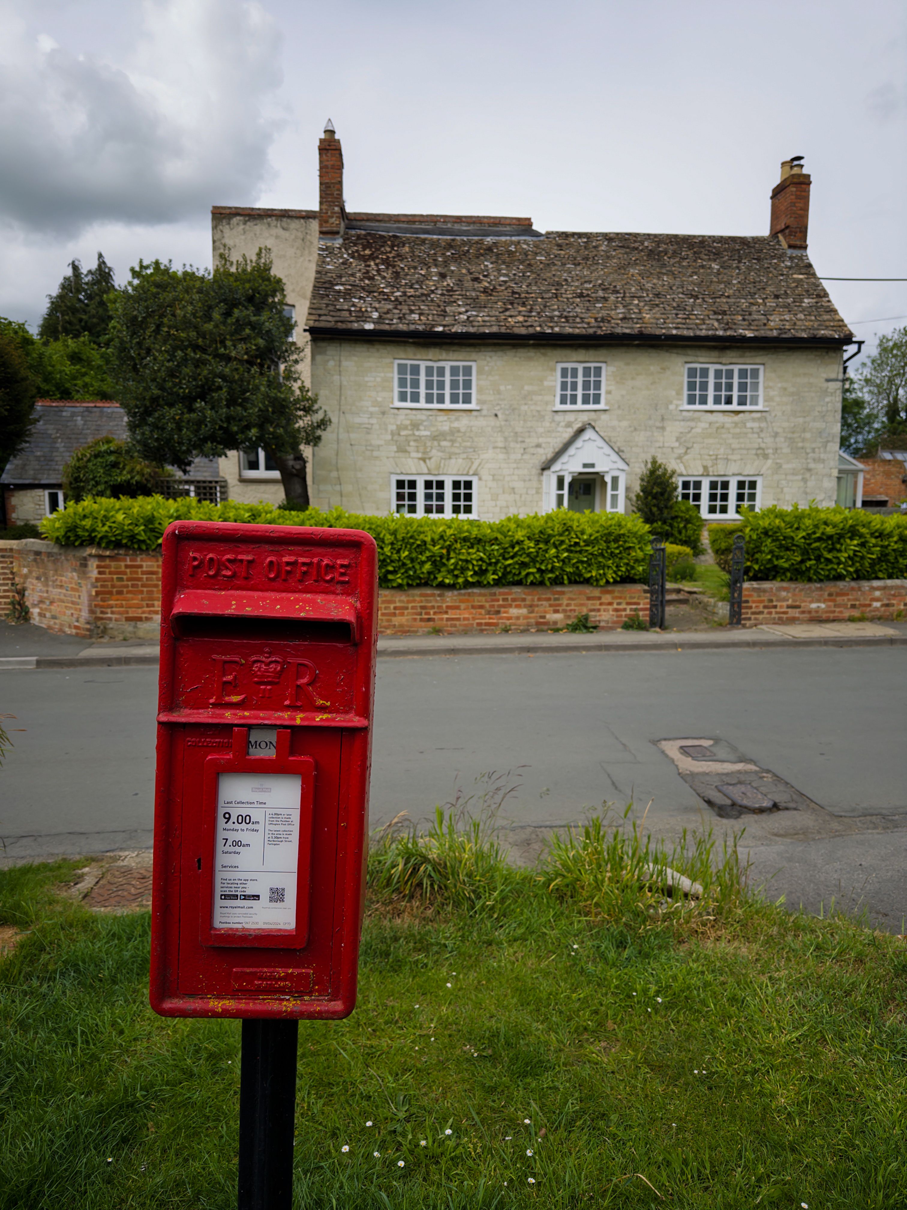 Red post box in front of a classic British countryside cottage, a serene outdoor scene.