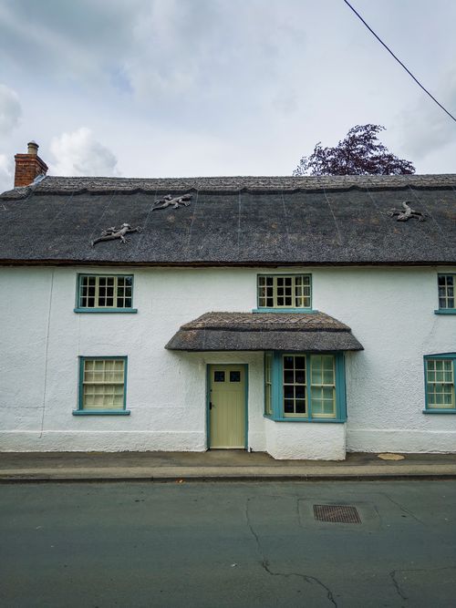 Free A picturesque thatched-roof cottage with unique decorations in a serene English village setting. Stock Photo